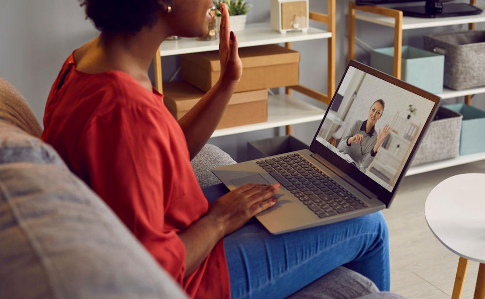 Woman sitting on a couch with a laptop, participating in a telehealth therapy session for ADHD symptoms in women