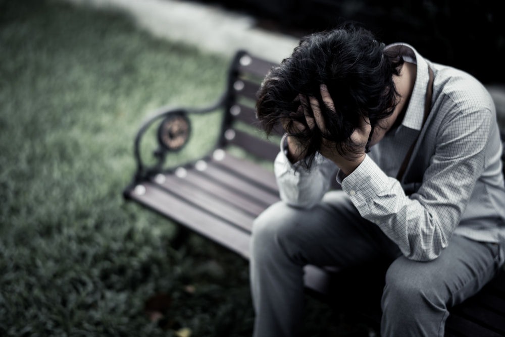 person sitting on a bench outdoors with their head in their hands experiencing bad trip