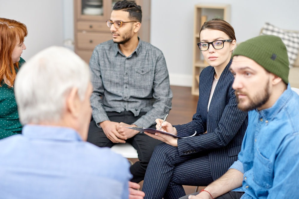 group of adults sitting in chairs, having a discussion in group therapy about bad trips.