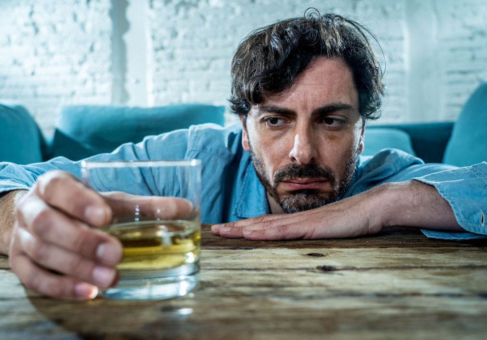 man struggling with alcohol withdrawal while looking at a glass of alcohol