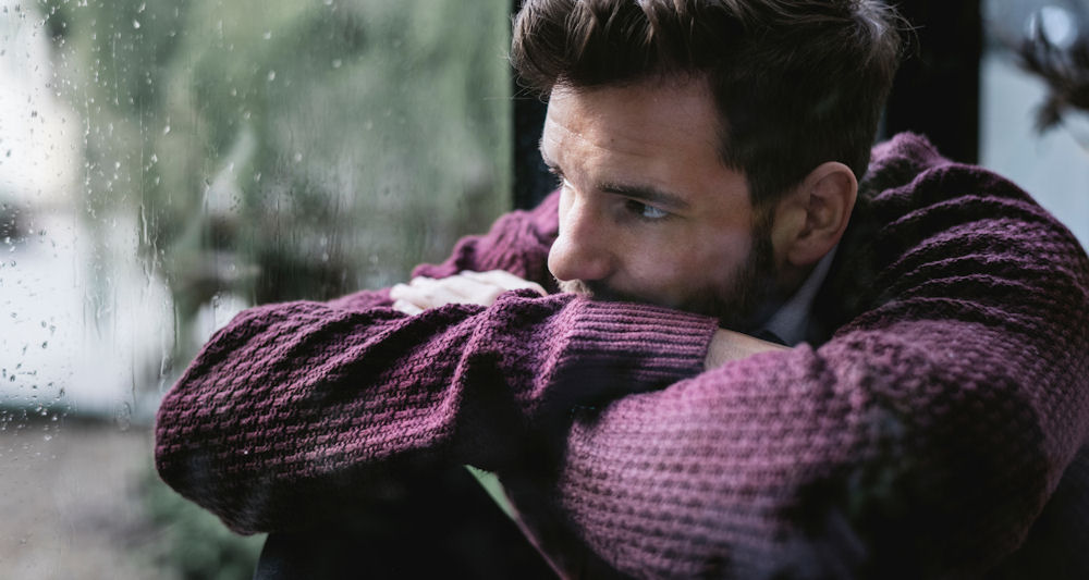 man staring out window, appearing depressed after using kratom, feeling low.
