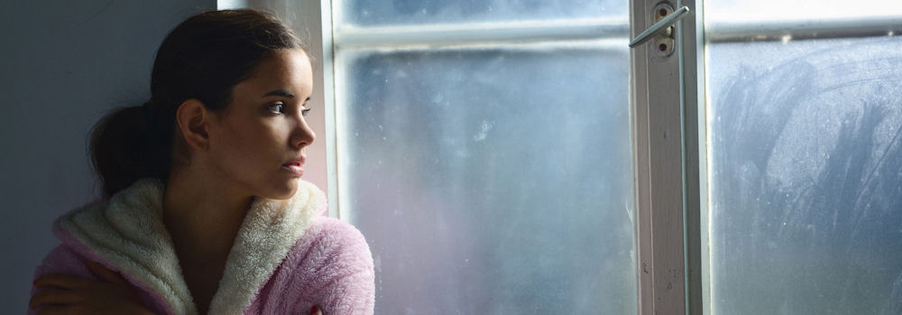 Young woman showing signs of high functioning anxiety while quietly reflecting by a window