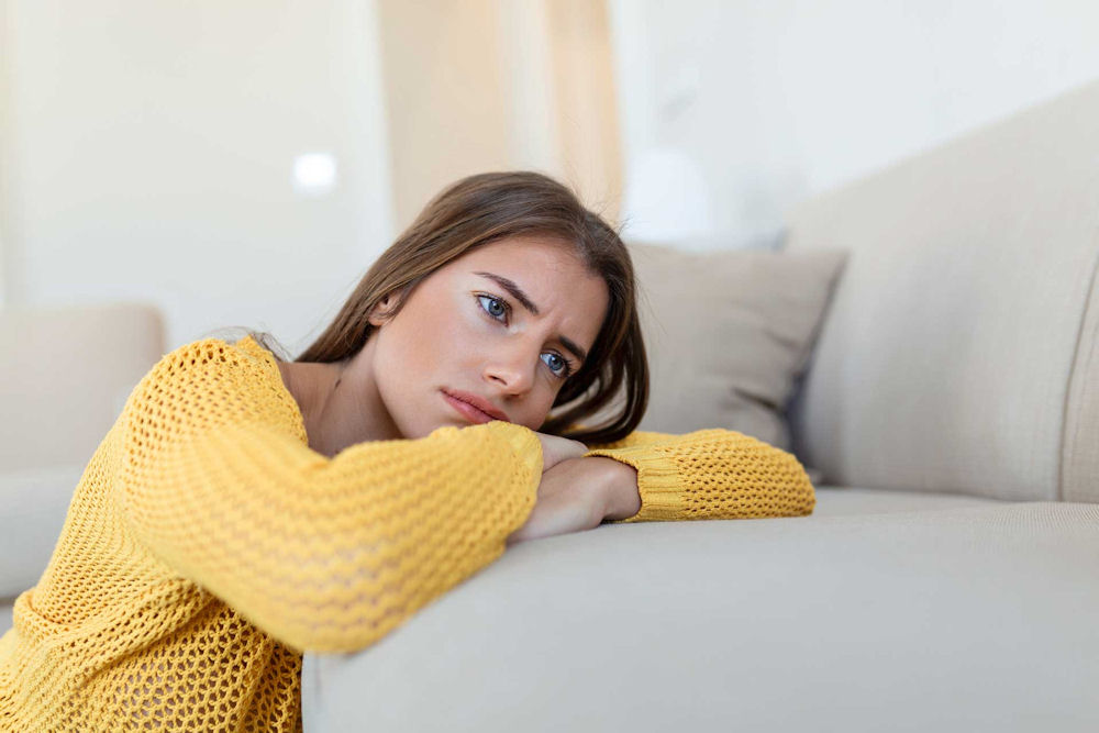Woman lying on a couch looking emotionally withdrawn, illustrating common symptoms of untreated depression such as sadness and emotional numbness.