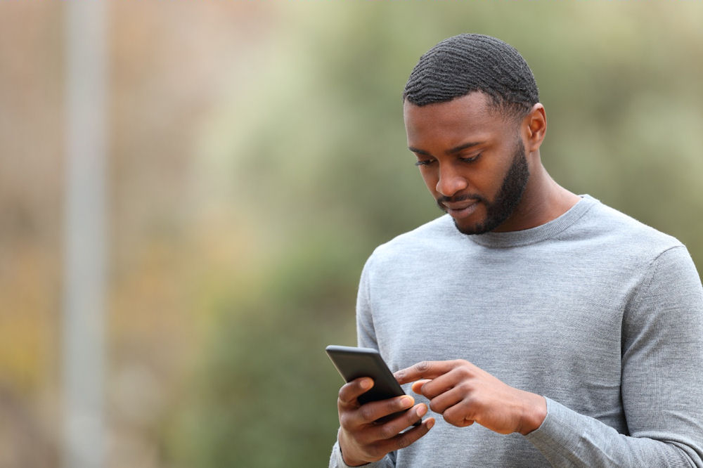 Man looking at his phone with a thoughtful expression, reflecting stress and self-criticism related to perfectionism and mental health.