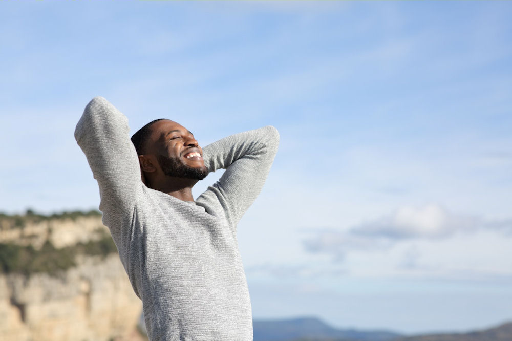 Man smiling with arms raised while outdoors, symbolizing balance, self-acceptance, and healing in perfectionism and mental health.