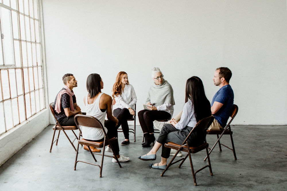 Group of people seated in a therapy circle participating in a discussion, depicting a group session in inpatient rehabilitation.